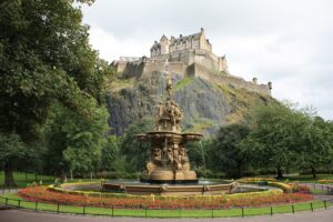Edinbugh castle on a rock with a fountain in front of it