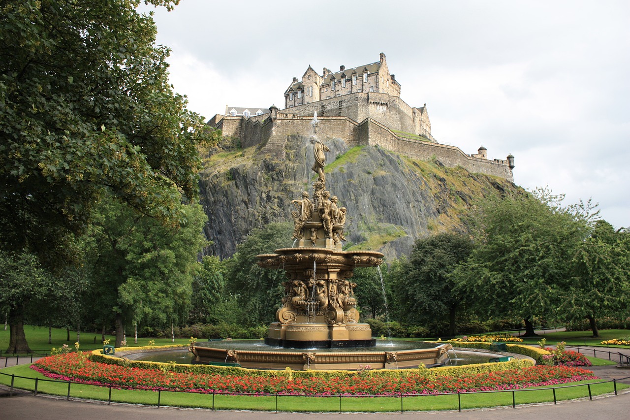 Edinbugh castle on a rock with a fountain in front of it