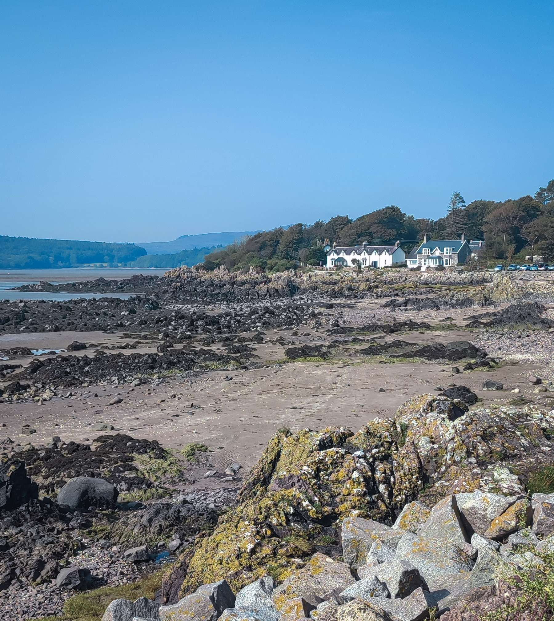A rocky beach with white cottages in the distance on a beautiful clear summers day