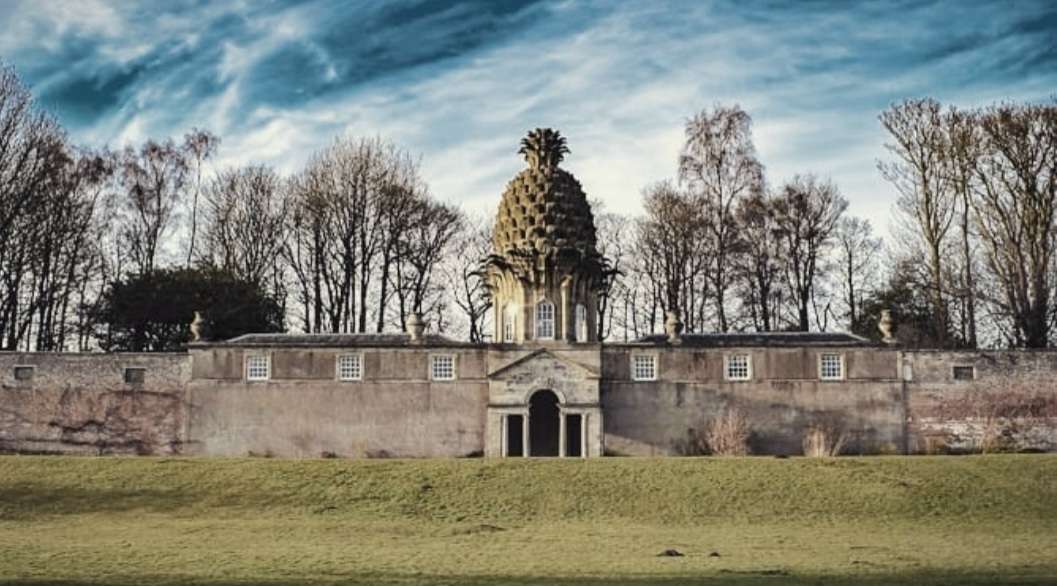 A quirky sandstone building with a pineapple dome build on top. Set in grassy grounds.