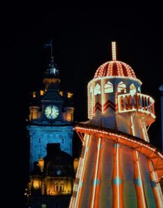Edinburgh showing a lit up christmas ride and clock tower in the background